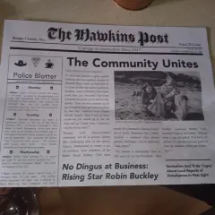 Gazeta "The Hawkins Post" z artykułem "The Community Unites" i zdjęciem dzieci sprzątających plażę.