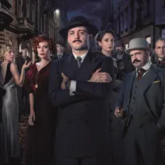 Grupa postaci w strojach z epoki, w tym mężczyzna z wąsami w garniturze, wygląda jak kadr z serialu Netflix.