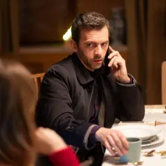 Mężczyzna przy stole rozmawia przez telefon, jakby był nieobecny, gdy w TV leci film.