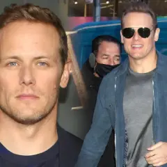 Sam Heughan, znany z roli w Outlander, w okularach przeciwsłonecznych i niebieskiej kurtce. W tle widać fragment logo i napis "covid testing".