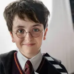 Chłopiec w okularach i szacie Hogwartu, trzymający klaps filmowy. Wygląda jak nowy Harry Potter, gotowy na przygodę.