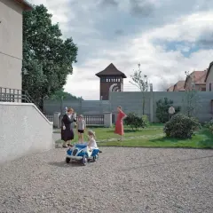 Strefa interesów recenzja: rodzina w ogrodzie, za nią mur, druty kolczaste i wieża strażnicza. Dzieci bawią się autem.