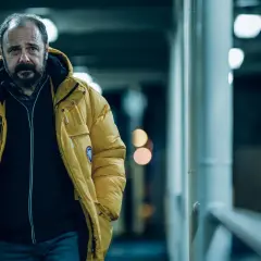 Mężczyzna w żółtej kurtce, zamyślony, idzie w stronę kamery. To kadr z filmu "Klangor", streszczenie szczegółowe tej sceny.