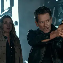 Kevin Bacon jako łowca nagród w serialu, z pistoletem w ręku, obok przerażonej kobiety.