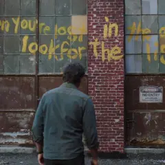 Joel patrzy na napis "When you're lost in the darkness, look for the light" na ścianie budynku, nawiązanie do świetlików z The Last of Us.