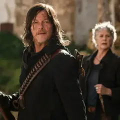 Daryl i Carol, bohaterowie seriali o zombie, przygotowują się do walki. Daryl trzyma strzelbę, a Carol stoi za nim.