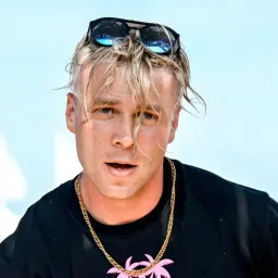 Młody mężczyzna z blond włosami i okularami na głowie, w czarnej koszulce ze złotym łańcuchem. Czy skolim grał w filmie?