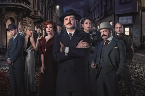 Grupa postaci w strojach z epoki, w tym mężczyzna z wąsami w garniturze, wygląda jak kadr z serialu Netflix.