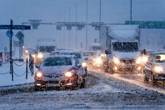 Pierwszy śnieg zasypał drogę, tworząc korki. Samochody z zapalonymi światłami powoli poruszają się po zaśnieżonej jezdni.