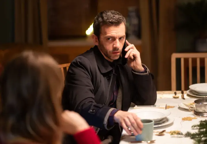 Mężczyzna przy stole rozmawia przez telefon, jakby był nieobecny, gdy w TV leci film.