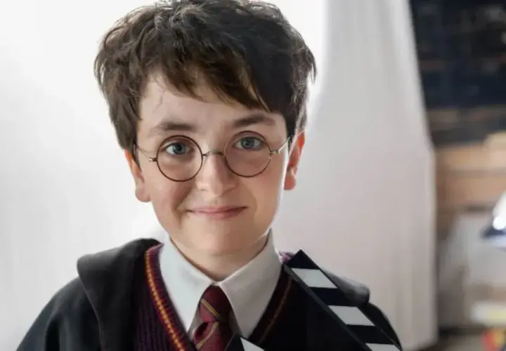 Chłopiec w okularach i szacie Hogwartu, trzymający klaps filmowy. Wygląda jak nowy Harry Potter, gotowy na przygodę.