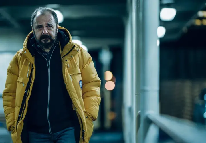 Mężczyzna w żółtej kurtce, zamyślony, idzie w stronę kamery. To kadr z filmu "Klangor", streszczenie szczegółowe tej sceny.