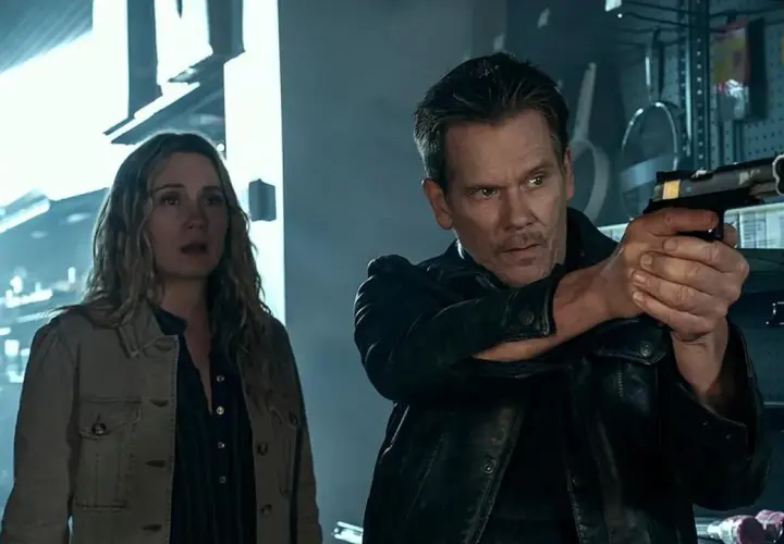 Kevin Bacon jako łowca nagród w serialu, z pistoletem w ręku, obok przerażonej kobiety.