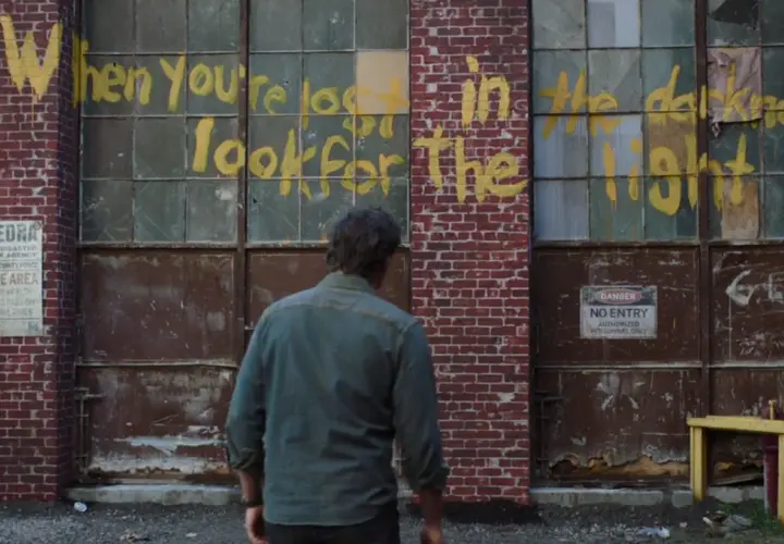 Joel patrzy na napis "When you're lost in the darkness, look for the light" na ścianie budynku, nawiązanie do świetlików z The Last of Us.
