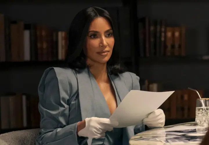 Kim Kardashian w eleganckim kostiumie i białych rękawiczkach czyta dokumenty, jakby przygotowywała się do roli w nowym serialu.