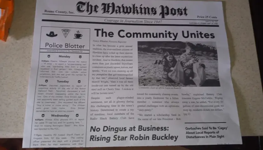 Gazeta "The Hawkins Post" z artykułem "The Community Unites" i zdjęciem dzieci sprzątających plażę.