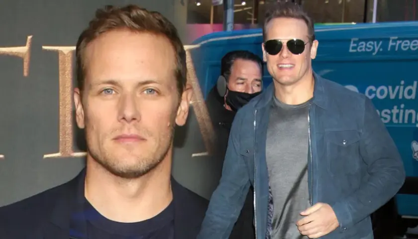 Sam Heughan, znany z roli w Outlander, w okularach przeciwsłonecznych i niebieskiej kurtce. W tle widać fragment logo i napis "covid testing".