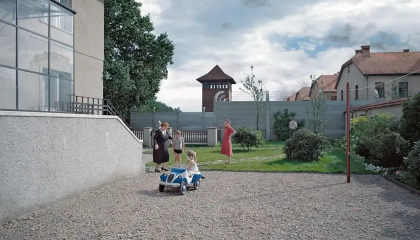 Strefa interesów recenzja: rodzina w ogrodzie, za nią mur, druty kolczaste i wieża strażnicza. Dzieci bawią się autem.