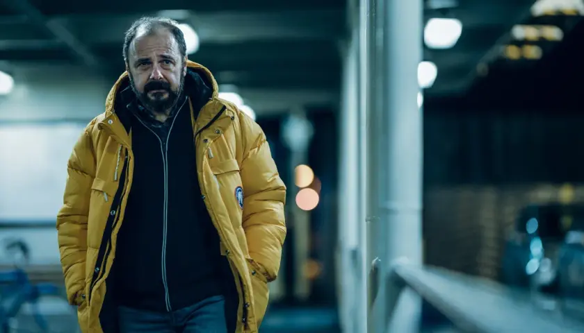 Mężczyzna w żółtej kurtce, zamyślony, idzie w stronę kamery. To kadr z filmu "Klangor", streszczenie szczegółowe tej sceny.
