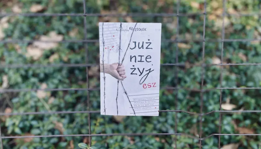 Okładka książki "Już nie żyjesz" Krzysztofa Koziołka, wisząca na płocie. Wstrząsająca historia, która skłania do myślenia, jak zasady przyjemności serial.
