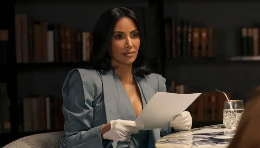 Kim Kardashian w eleganckim kostiumie i białych rękawiczkach czyta dokumenty, jakby przygotowywała się do roli w nowym serialu.
