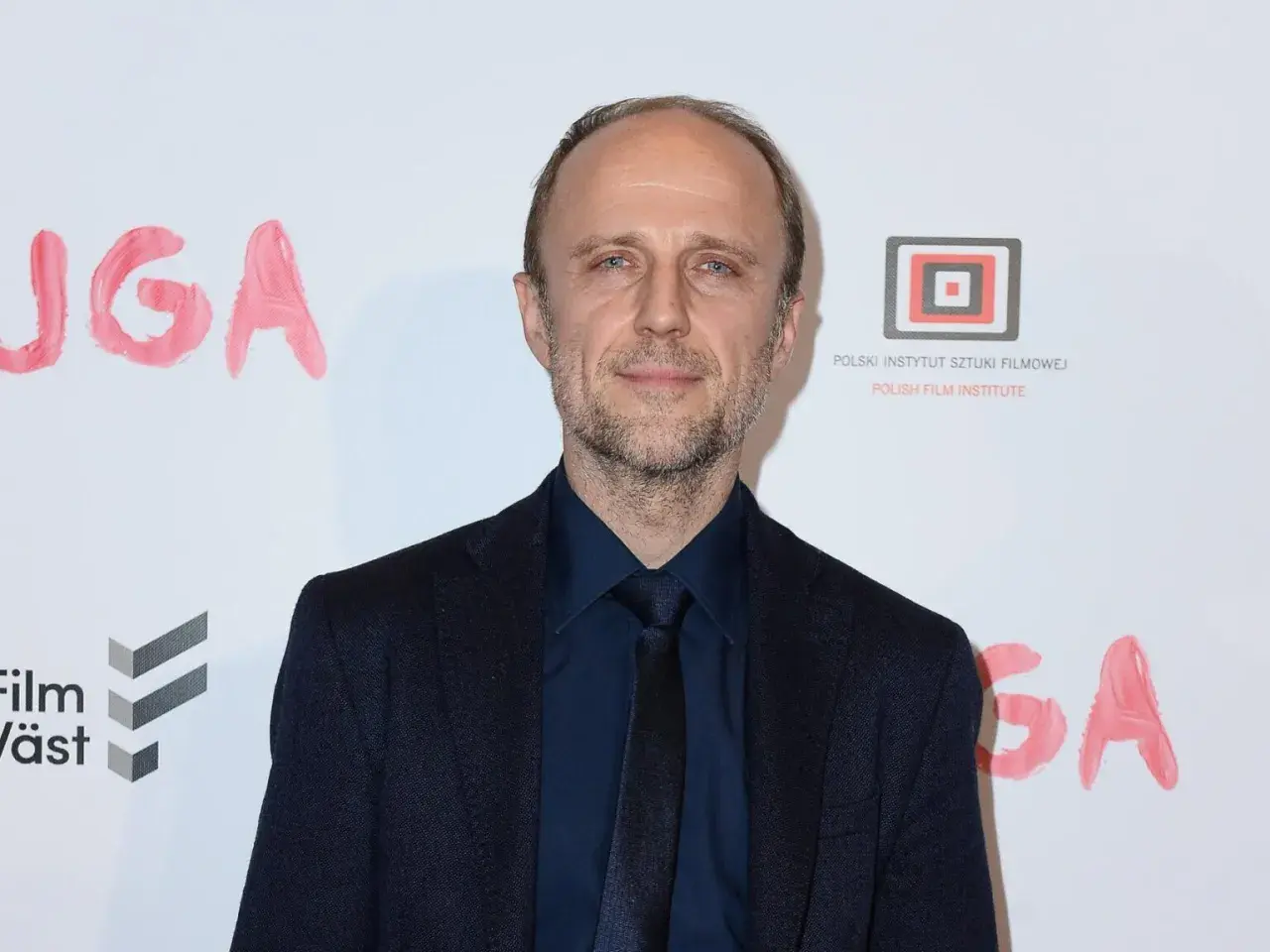Łukasz Simlat, znany z wielu ról filmowych, na tle napisu "JUGA".
