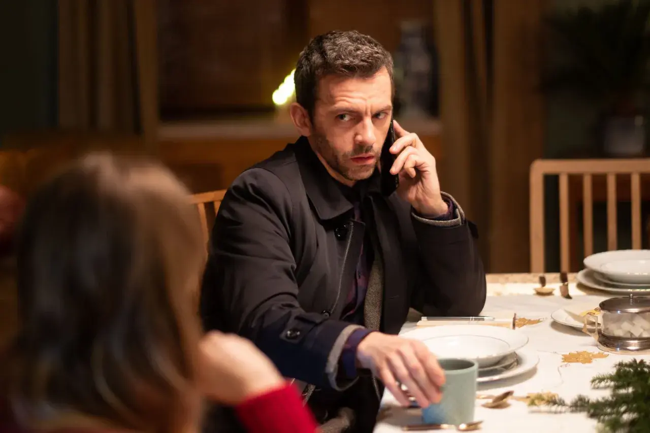 Mężczyzna przy stole rozmawia przez telefon, jakby był nieobecny, gdy w TV leci film.