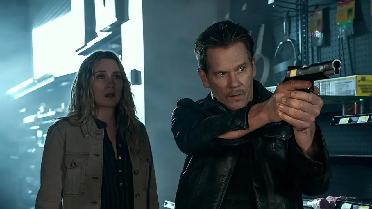 Kevin Bacon jako łowca nagród w serialu, z pistoletem w ręku, obok przerażonej kobiety.