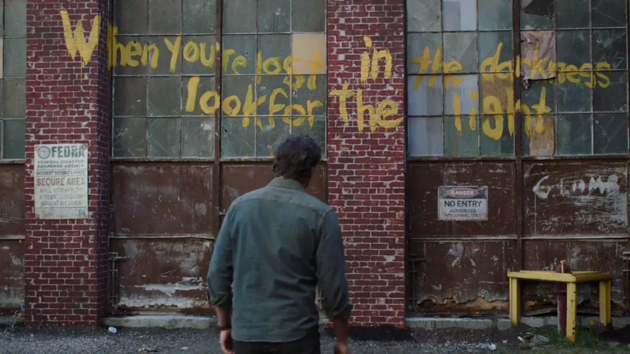 Joel patrzy na napis "When you're lost in the darkness, look for the light" na ścianie budynku, nawiązanie do świetlików z The Last of Us.