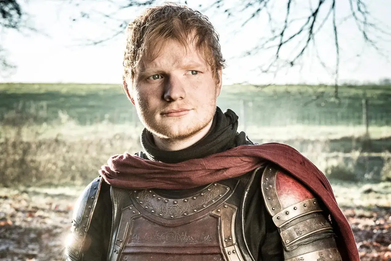Ed Sheeran w zbroi, jakby z Gry o Tron, patrzy w bok na tle jesiennego krajobrazu.