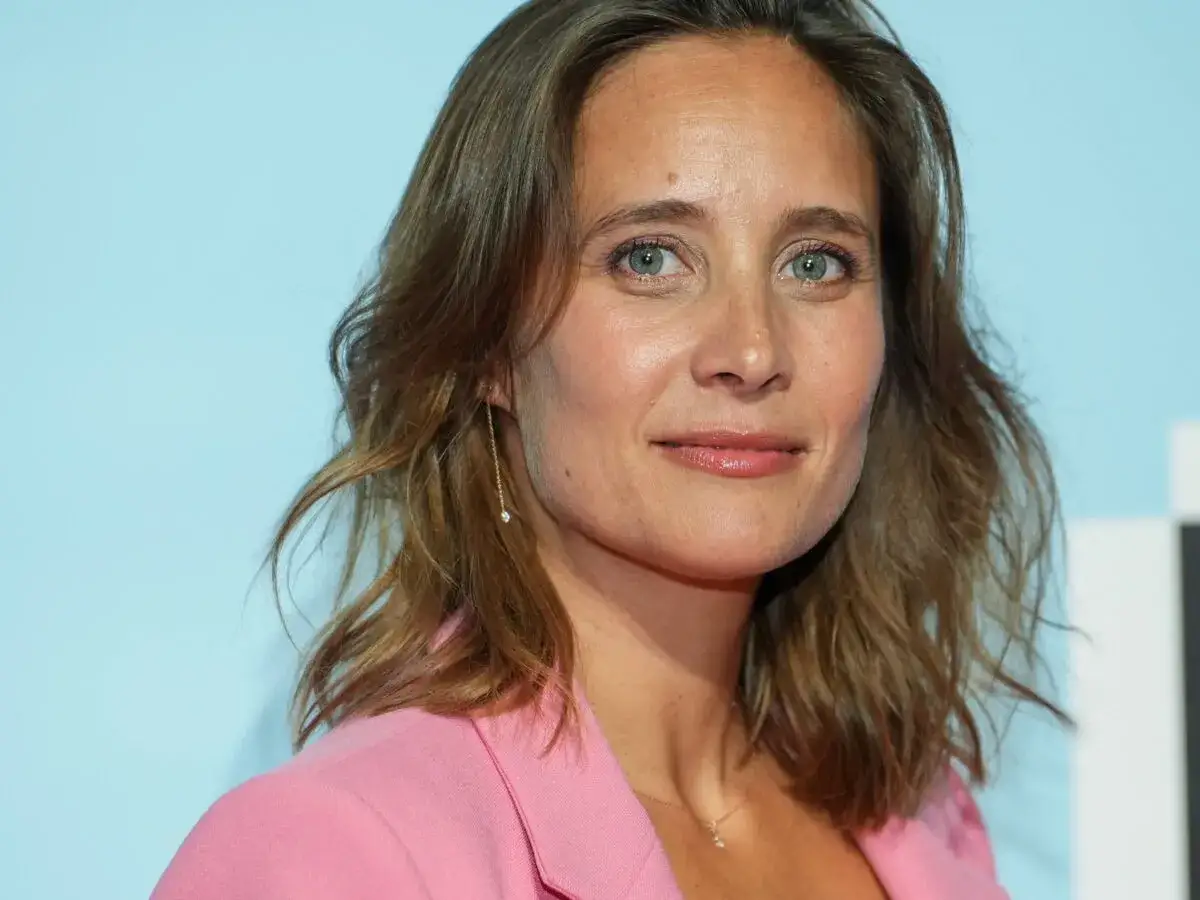 Portret Julie de Bona w różowej marynarce, z delikatnym uśmiechem i niebieskimi oczami.
