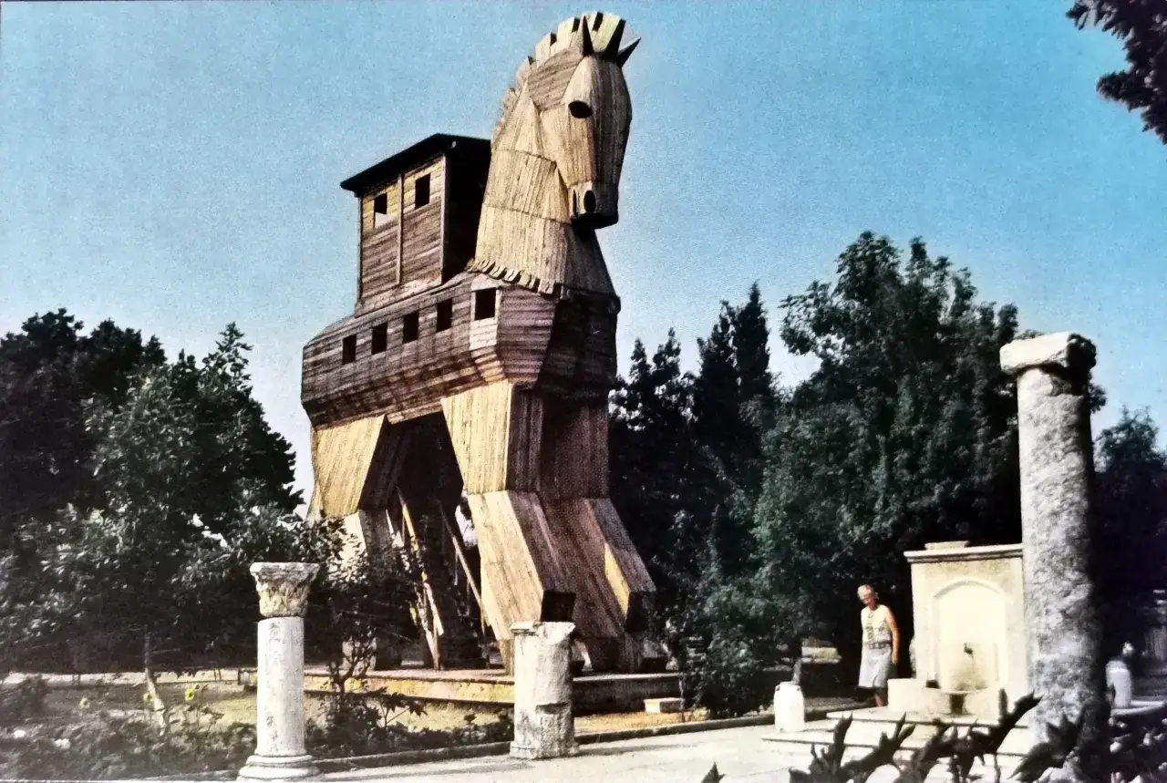 Drewniany koń, symbol podstępu i klęski Troi, stoi na tle drzew i ruin.
