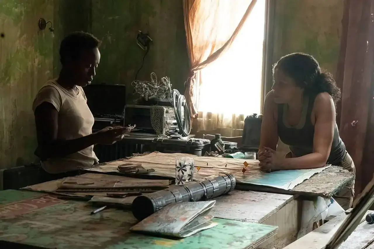 Dwie kobiety planują podróż w zrujnowanym pokoju, jak w The Last of Us. Na stole leżą mapy i dziwny przedmiot, przypominający świetliki.