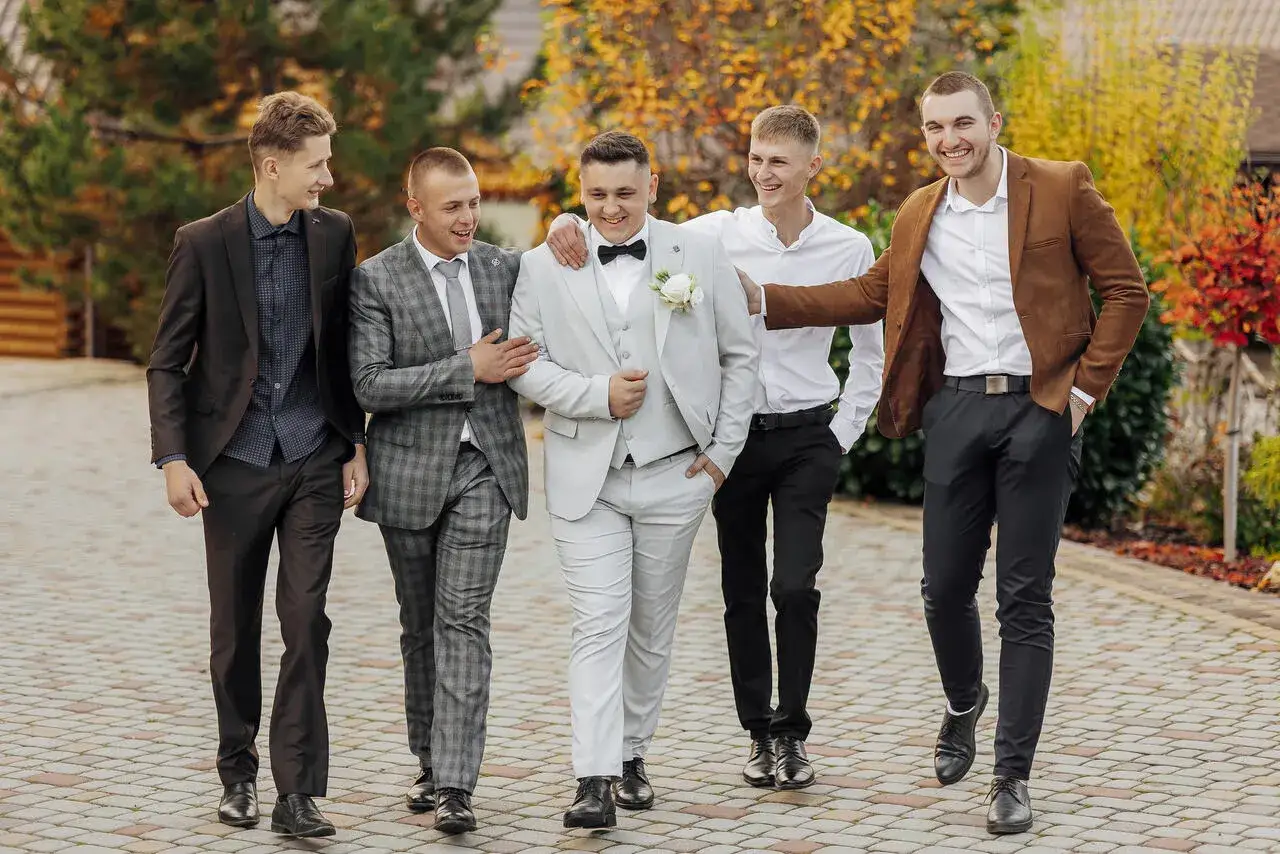 Pięciu mężczyzn w garniturach idzie razem, śmiejąc się i rozmawiając.