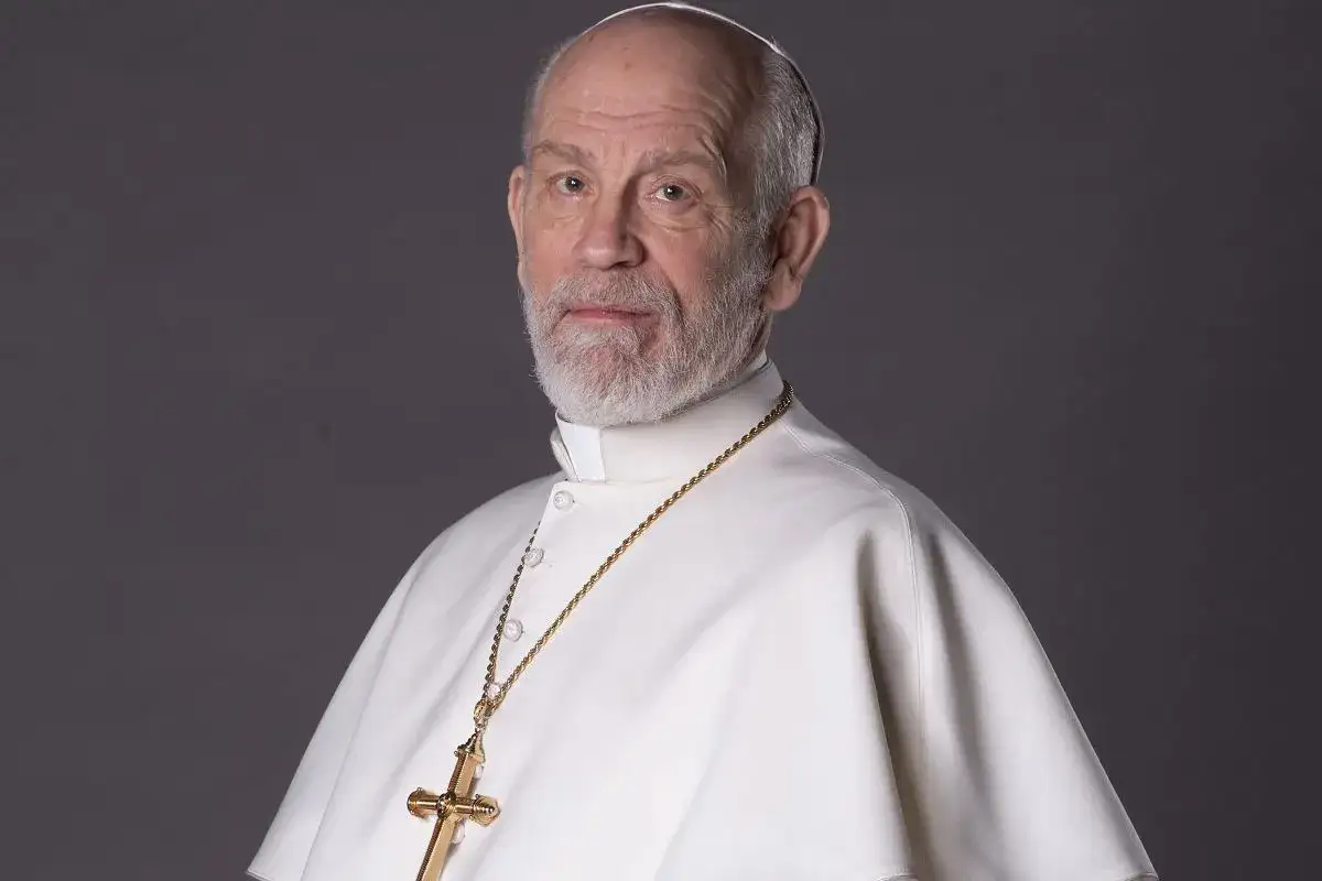 John Malkovich jako nowy papież w serialu, w białej szacie i złotym krzyżu.
