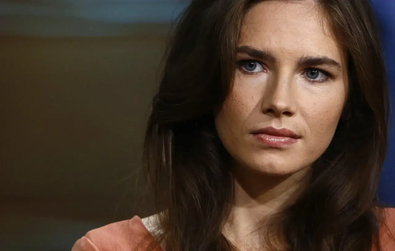 Zbliżenie na twarz Amandy Knox, której sprawa wstrząsnęła światem. Jej niebieskie oczy patrzą w dal, a ciemne włosy opadają na ramiona.